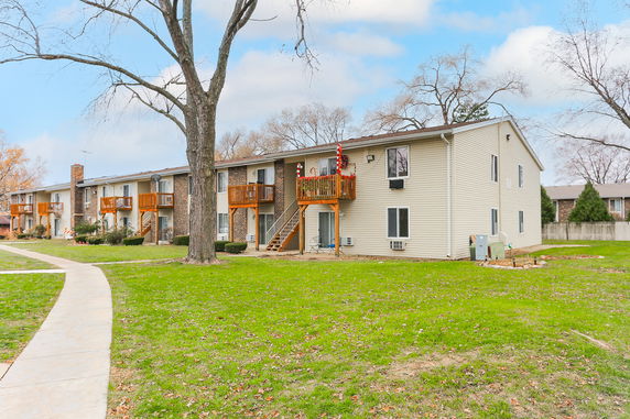 Front view of a multi-unit residential building with balconies and a tree in the foreground.