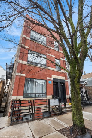 Front view of a three-story brick building with large windows and a tree in the foreground.