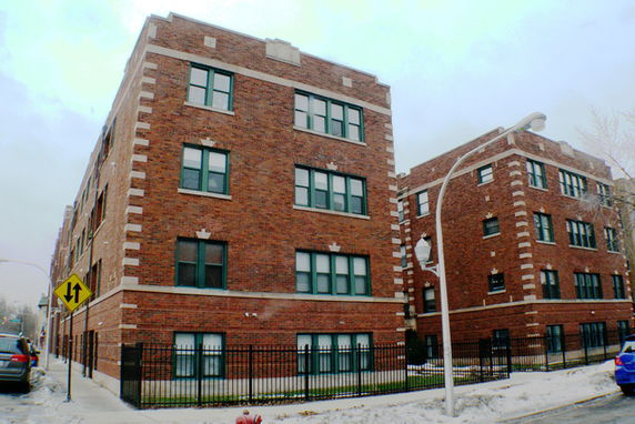 Front view of a brick apartment building with multiple floors and green-framed windows.