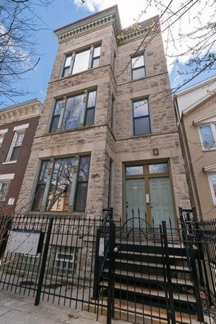 Front view of a multi-story stone house with large windows.