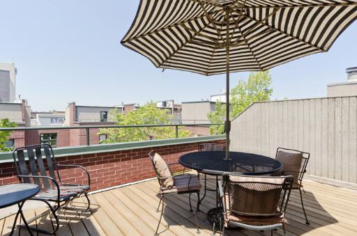 Rooftop patio with chairs, a table, and a striped umbrella.