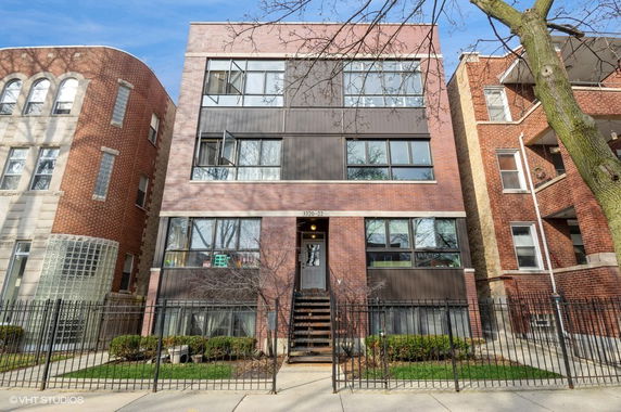 Front view of a three-story brick building with wide windows and a central entrance with stairs.