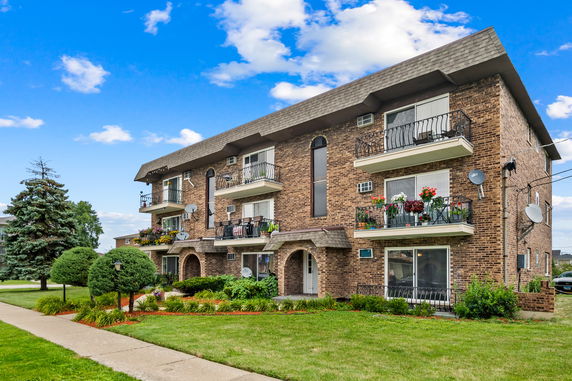 Front view of a three-story brick building with balconies and decorative plants.