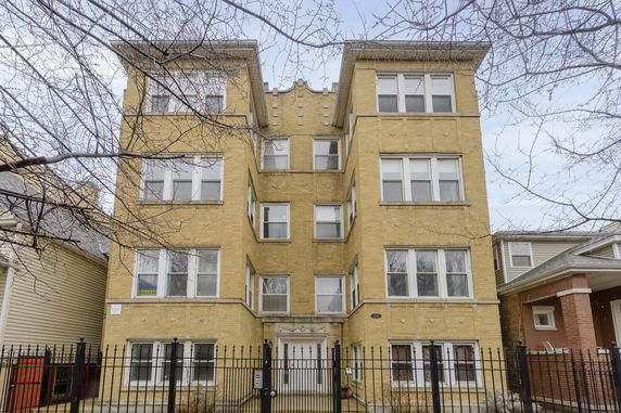 Front view of a three-story brick apartment building with multiple windows and a gated entrance.