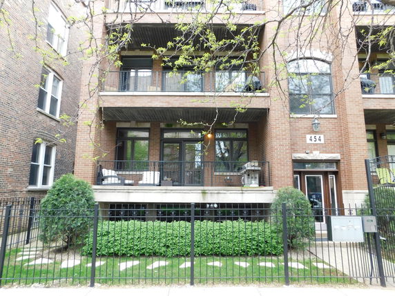 Front view of a multi-story brick building with balconies and a fenced entrance.