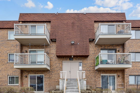 Front view of a multi-story brick apartment building with balconies and a central entrance.