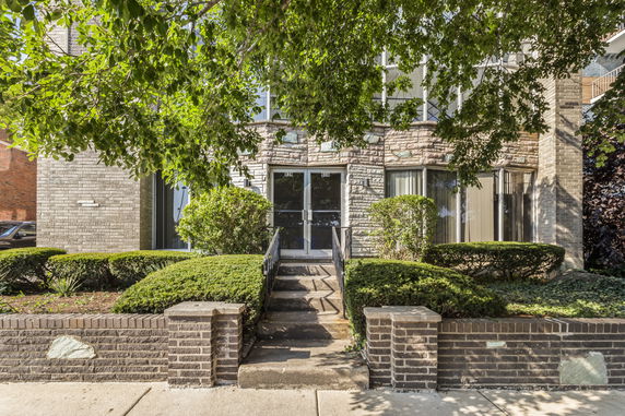 Front view of a building entrance with stone facade and shrubbery.