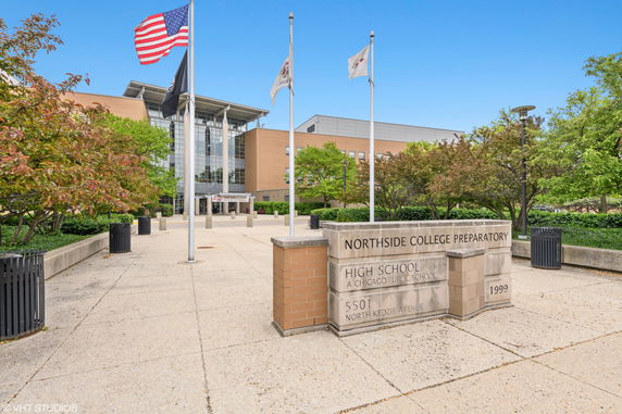 Front view of a modern, multi-story building with large glass windows and flagpoles.