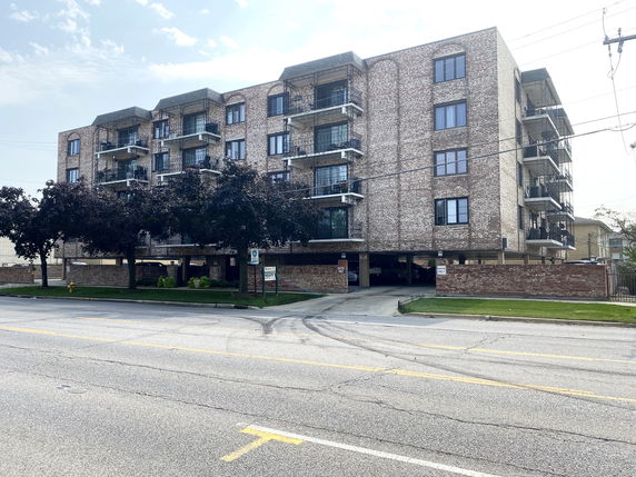 Front view of a multi-story brick apartment building with balconies and covered parking area.