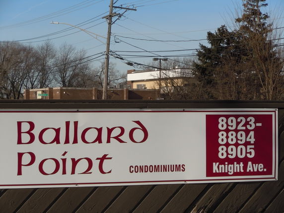 Front view of the Ballard Point Condominiums sign with buildings in the background.