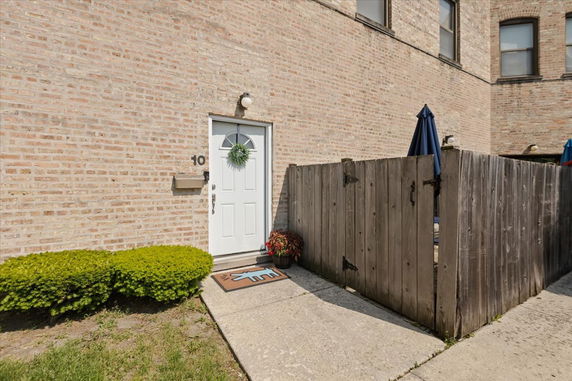 Front view of a brick building with a white door and a small fenced patio area.