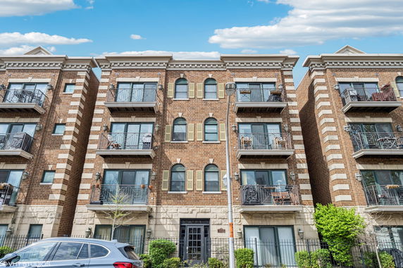 Front view of a multi-story brick apartment building with balconies and arched windows.