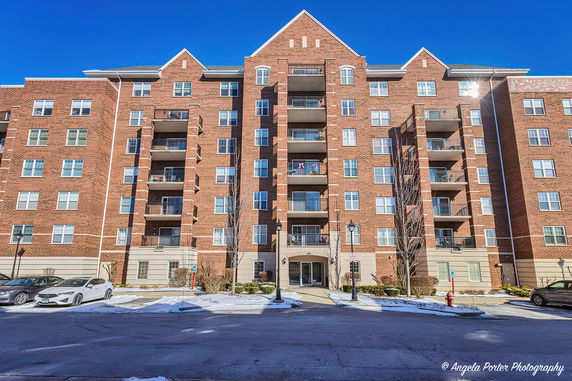 Front view of a multi-story brick residential building with balconies and parked cars.