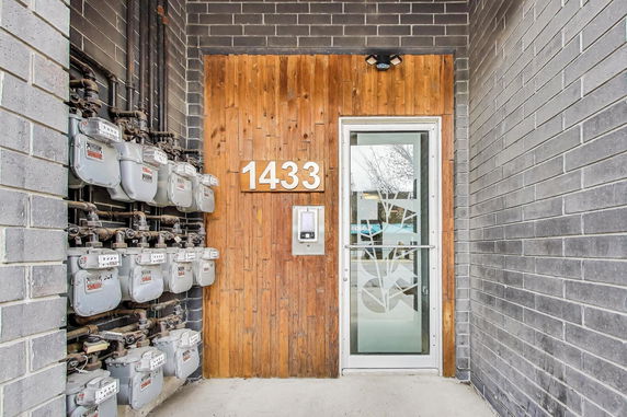 Entrance of a building with a wooden panel featuring the number 1433 and multiple utility meters on the side wall.