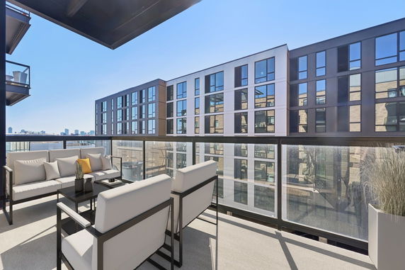 Outdoor seating area on a balcony with modern apartment buildings and city skyline in the background.
