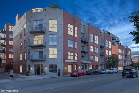Front view of a multi-story apartment building with balconies and large windows.