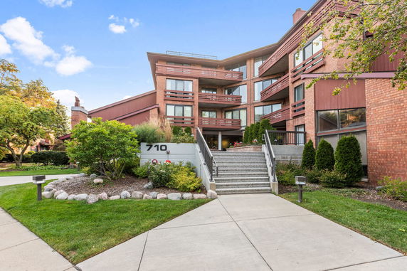 Front view of a multi-story apartment building with balconies and a staircase leading up to the entrance.