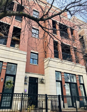 Front view of a multi-story brick building with black metal railings on balconies and large windows.