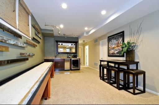 Interior room with a shuffleboard table and high-top stools, decorated with wall art and lighting.