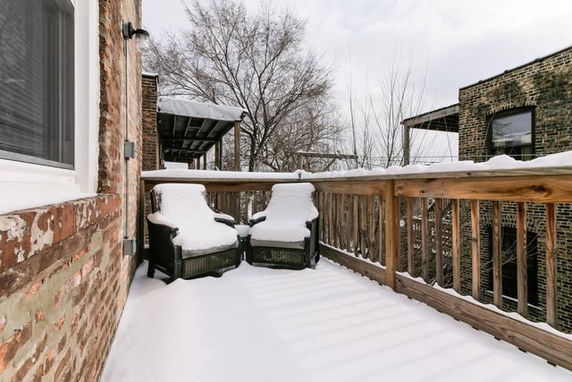 Snow-covered porch with chairs and view of neighboring building.