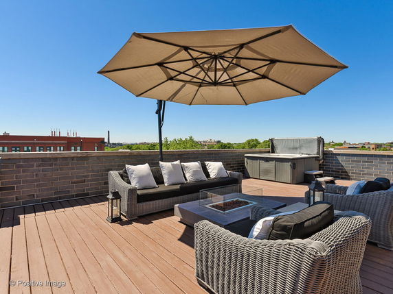Rooftop with wicker furniture, large umbrella, and a hot tub.