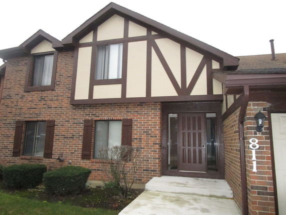 Front view of a two-story brick house with a wooden door and Tudor-style accents.