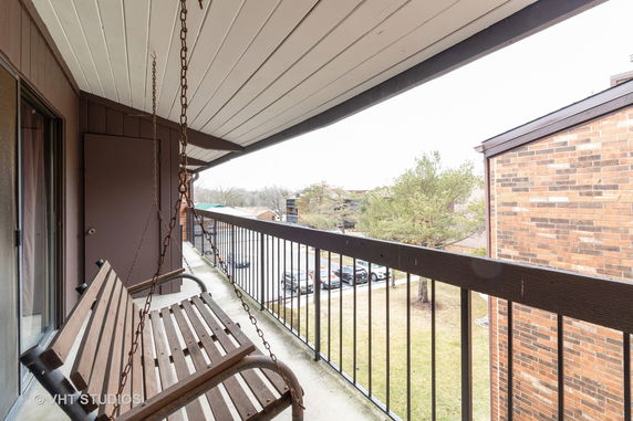 View from a balcony with a hanging swing, overlooking a parking area and nearby buildings.