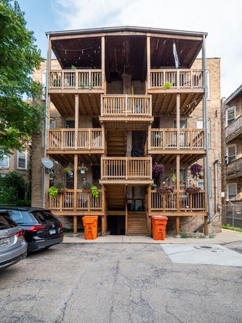 Rear elevation view of a three-story apartment building with wooden balconies and staircases.