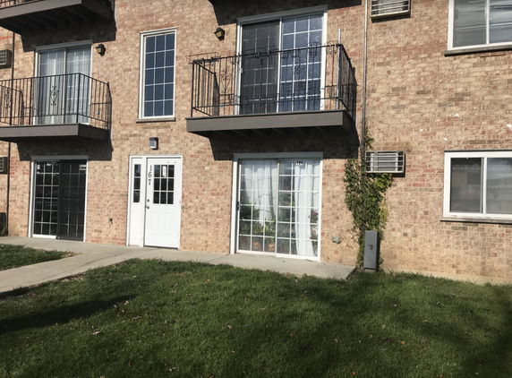 Front view of a brick apartment building with balconies and a white entrance door.