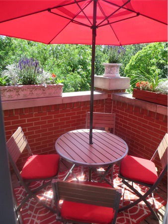 Patio area with red umbrella, round table, and chairs.