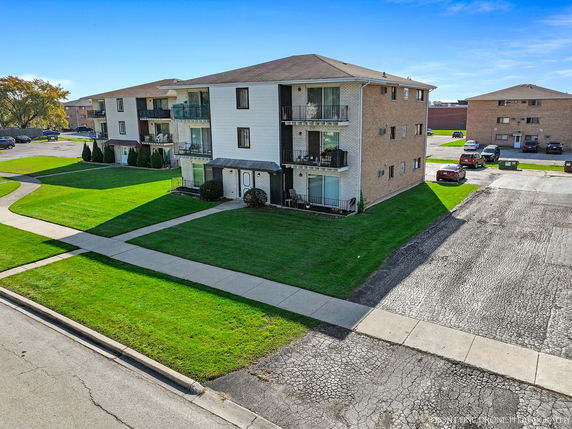 Front view of a three-story apartment building with balconies and green lawn.