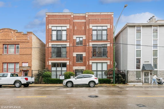 Front view of a multi-story brick building with large windows and a small fenced garden area.