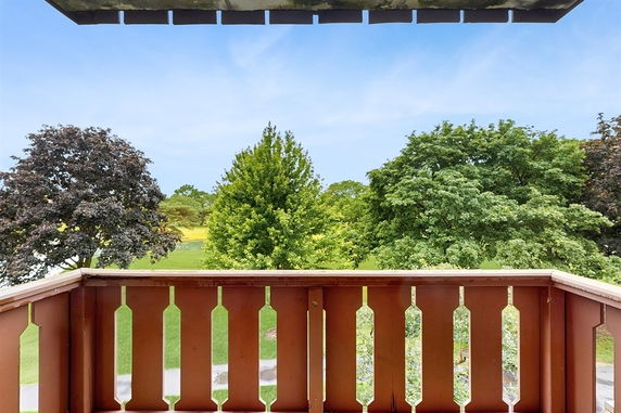 View from a balcony overlooking lush green trees and a grassy area.