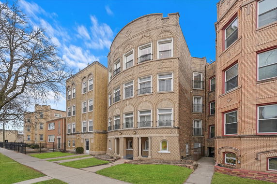 Front view of a multi-story apartment building with arched windows and decorative brickwork.