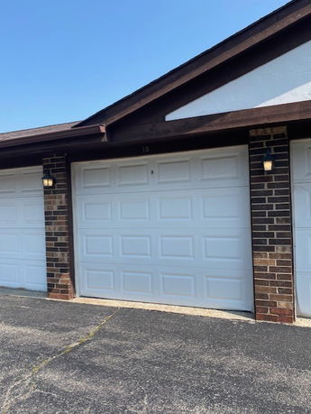 Front view of a building featuring a white garage door with brick detailing and exterior lighting.