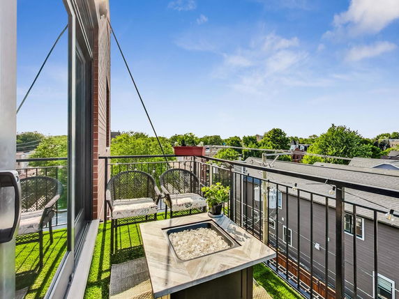 Panoramic view from a balcony overlooking residential rooftops and greenery.