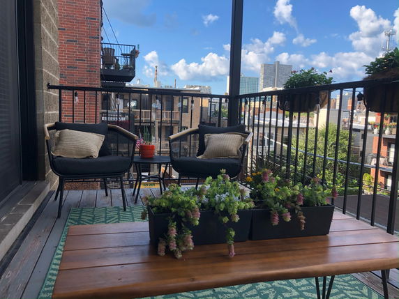 Balcony with chairs and plants overlooking cityscape.
