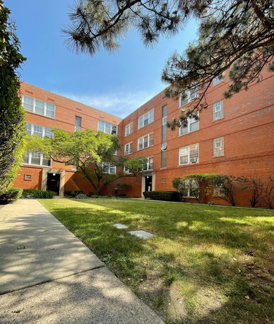 Front view of a red brick apartment building with multiple windows and entrance doors.