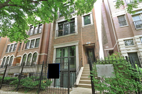 Front view of a multi-story brick building with balconies and a gated entrance.