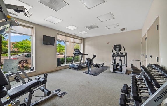 Indoor gym with various exercise equipment and large windows.