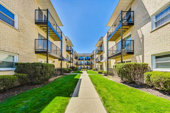 Front view of a multi-story apartment building with balconies and a landscaped walkway.