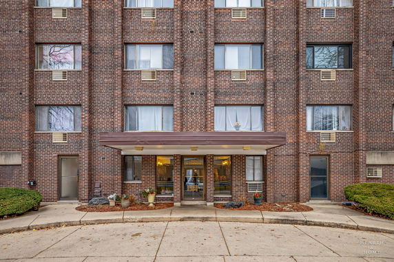 Front view of a multi-story brick building with a central entrance and several windows.