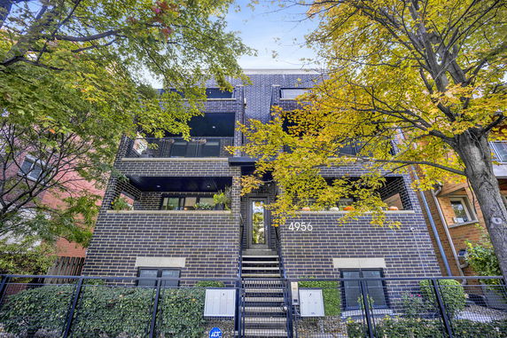 Front view of a multi-story brick building with balconies and a central entrance staircase.