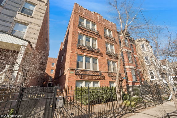 Front view of a multi-story brick building with balconies and a gated entrance.