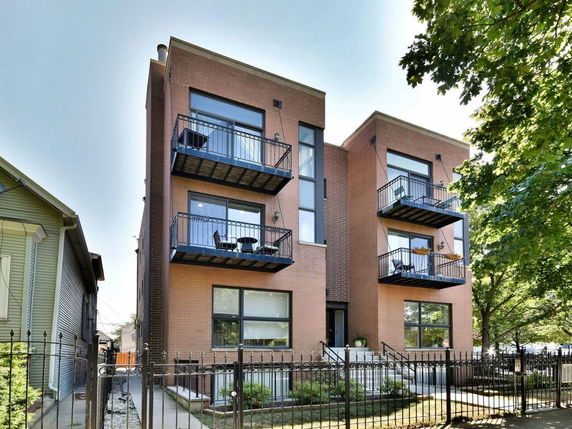 Front view of a multi-story brick building with balconies and a wrought iron fence.