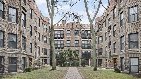 Front view of a multi-story brick apartment building with multiple windows and a courtyard.