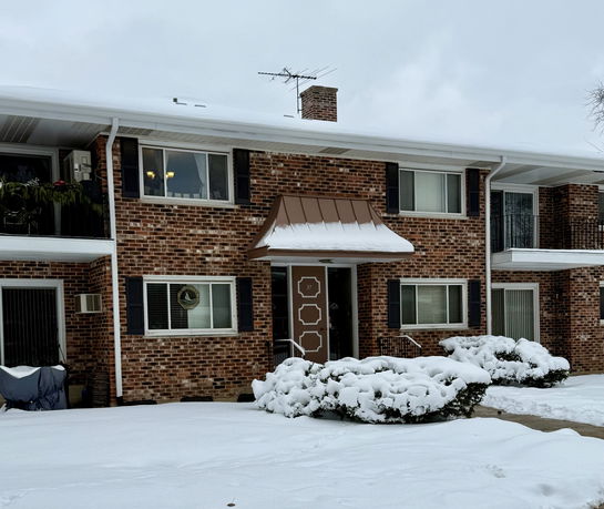 Front view of a two-story brick house with snow-covered roof and shrubs.