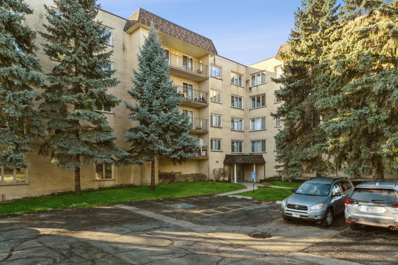 Front view of a multi-story residential building with balconies and small parking area.