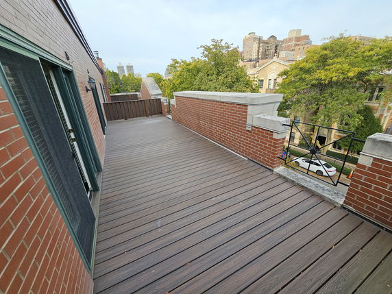 Rooftop with wooden decking and building view, featuring a railing and adjacent structures.