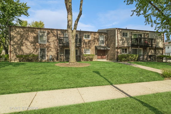 Front view of a two-story brick residential building with balconies and entrance canopy.